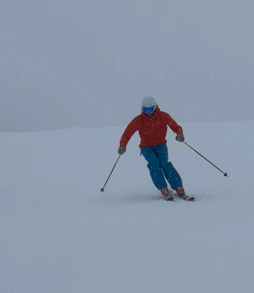 Skier in a red jacket and blue trousers turning on a snowy slope